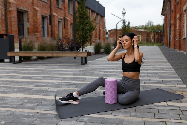 Pretty fitness woman sits on a mat and put on headphones on her head