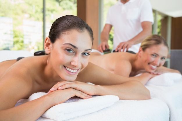 Pretty friends lying on massage tables with hot stones on their backs