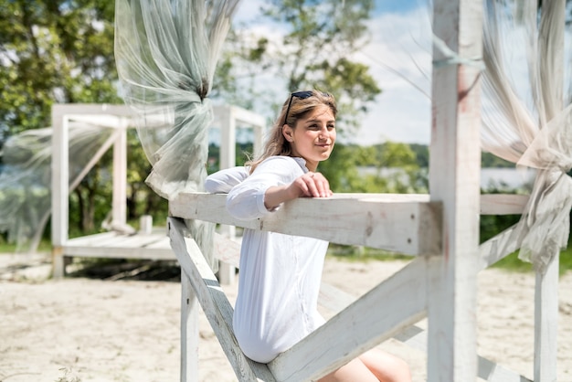 Pretty girl enjoy sunny summer day near lake in white gazebo