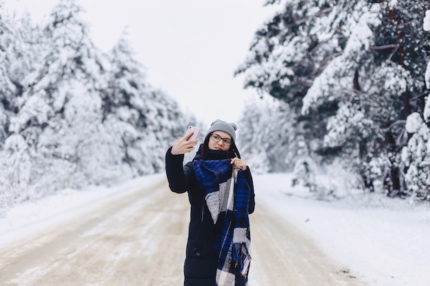 A pretty girl makes a selfie in the middle of a snowy forest road