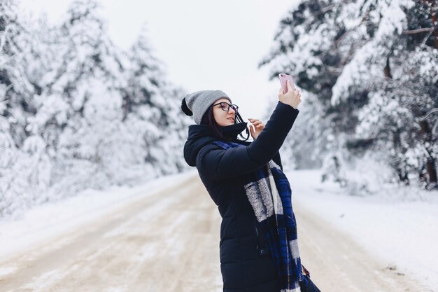 A pretty girl makes a selfie in the middle of a snowy forest road