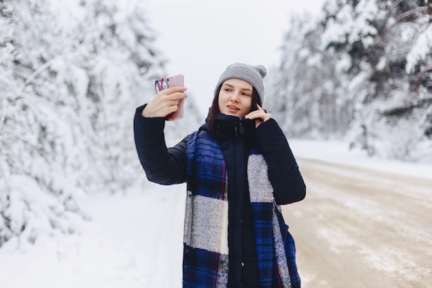 A pretty girl makes a selfie in the middle of a snowy forest road