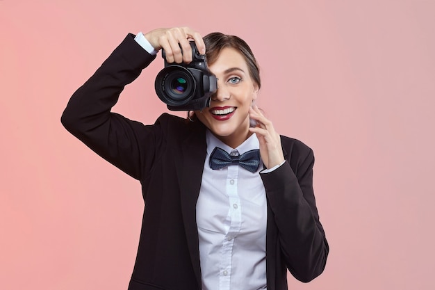 Pretty girl photographer in a men's suit and retro hairstyle on a pink background