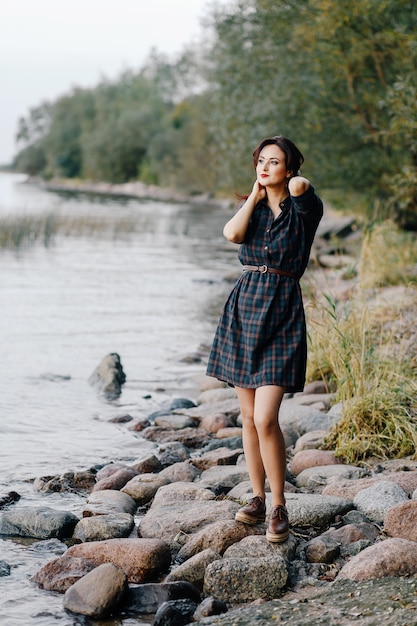 Pretty girl in a plaid dress is standing on the seashore