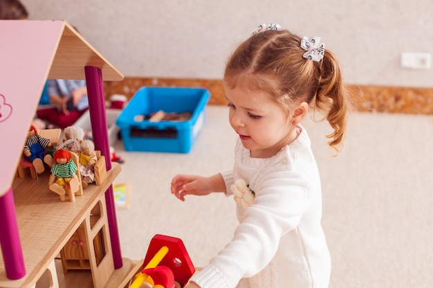 Pretty girl repairs the roof of dollhouse in the kindergarten