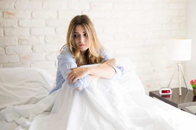 Pretty girl sitting on her bed in the morning and looking worried