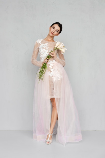 Pretty girl in transparent tulle dress with lace posing with flowers in hand