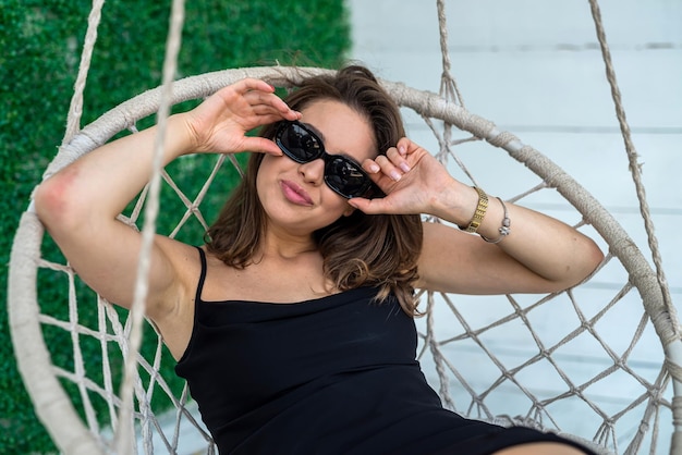 Pretty girl wear elegant black dress is sitting in a rocking chair outdoor or studio shot