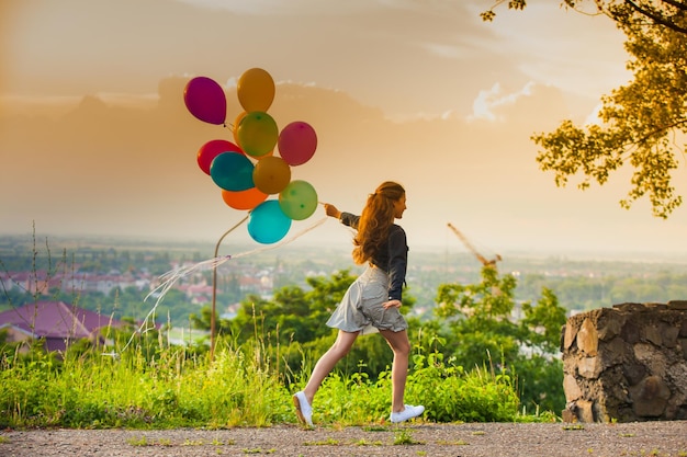 Pretty girl with big colorful balloons walking on the hills near the town