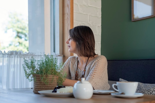 Pretty girl with cup of coffee in cafe in front of the window Young woman sitting in cafeteria and waiting for someone