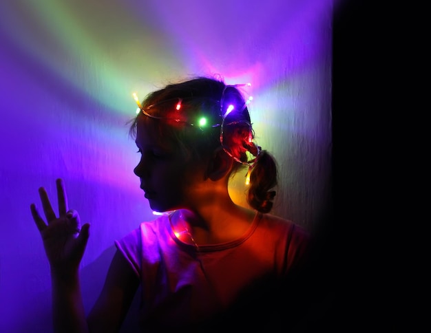 Pretty girl with garland on her hair on light rough illuminated wall background