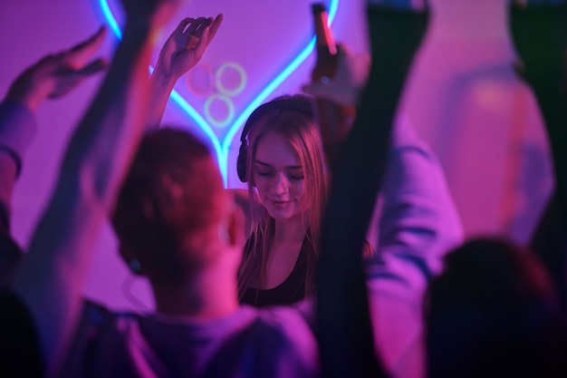 Pretty girl with long blond hair standing by counter with turntables while mixing music for disco dancing and enjoying at home party with friends