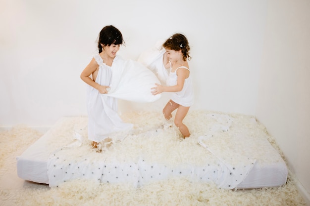 Pretty girls having pillows fight on mattress