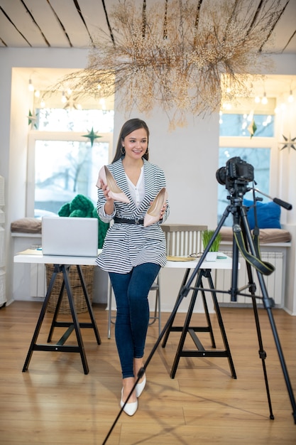 Pretty good looking woman standing with the shoes in front of the camera while speaking about her giveaway