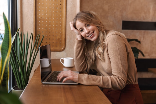 pretty happy girl sitting in cafe using laptop computer