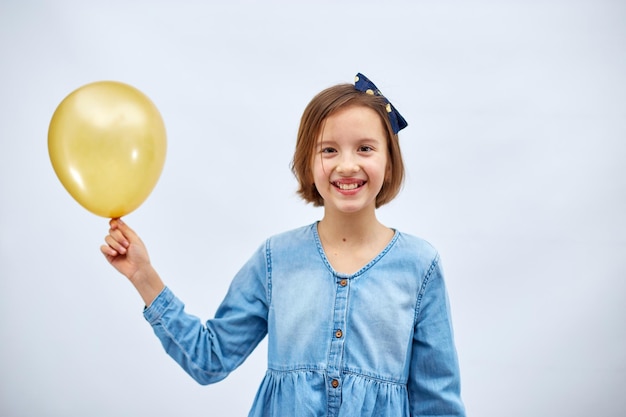 Pretty happy little girl in casual denim dress hold in hand yellow balloon