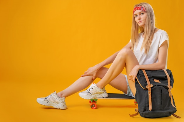 Pretty happy woman casually dressed sits on her skateboard 