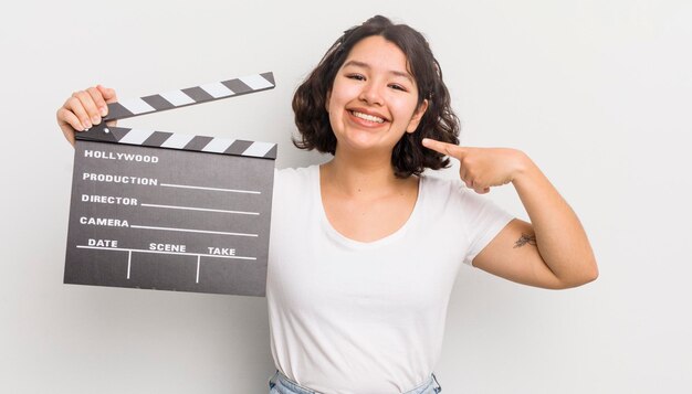 Pretty hispanic girl smiling confidently pointing to own broad smile cinema concept