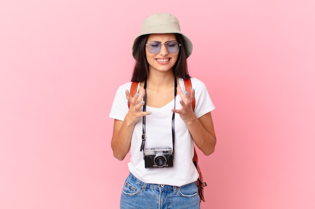 Pretty hispanic tourist looking desperate, frustrated and stressed with a photo camera and a hat