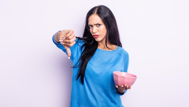 Pretty hispanic woman feeling cross,showing thumbs down. empty bowl concept