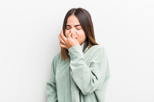 Pretty hispanic woman feeling disgusted holding nose to avoid smelling a foul and unpleasant stench