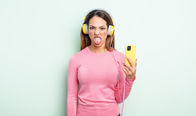 Pretty hispanic woman feeling disgusted and irritated and tongue out. smartphone and headphones concept