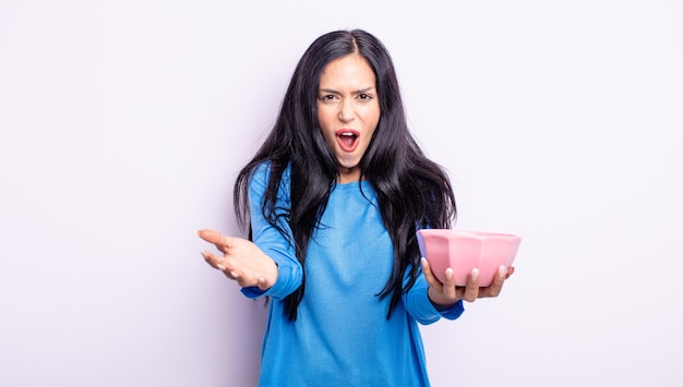 Pretty hispanic woman feeling extremely shocked and surprised. empty bowl concept