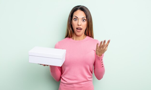 Pretty hispanic woman feeling extremely shocked and surprised. white box packaging concept