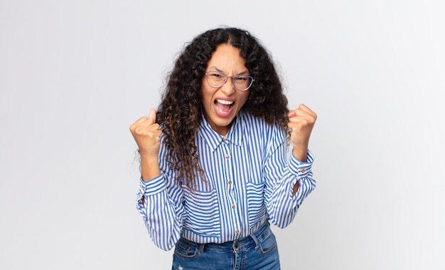 Pretty hispanic woman feeling happy, surprised and proud, shouting and celebrating success with a big smile