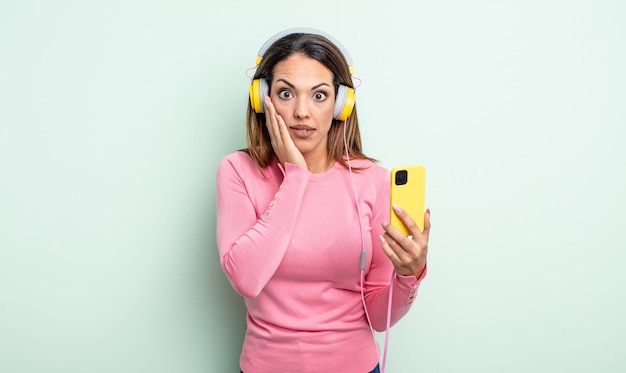 Pretty hispanic woman feeling shocked and scared. smartphone and headphones concept