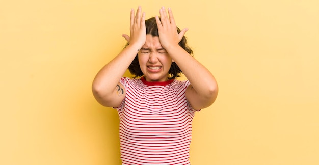 Pretty hispanic woman feeling stressed and anxious depressed and frustrated with a headache raising both hands to head