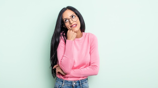 Pretty hispanic woman feeling thoughtful, wondering or imagining ideas, daydreaming and looking up to copy space