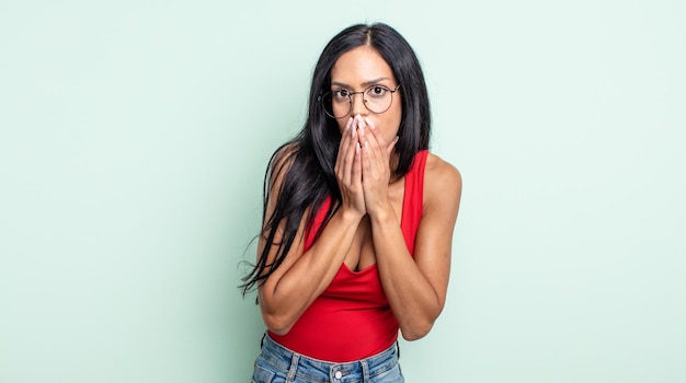 Pretty hispanic woman happy and excited, surprised and amazed covering mouth with hands, giggling with a cute expression