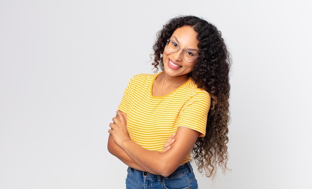 Pretty hispanic woman laughing happily with arms crossed, with a relaxed, positive and satisfied pose