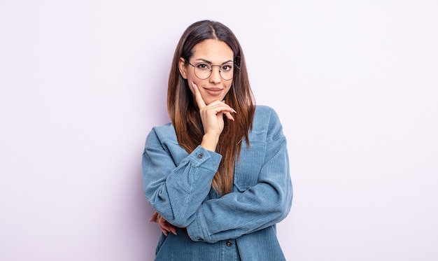 Pretty hispanic woman looking serious, thoughtful and distrustful, with one arm crossed and hand on chin, weighting options