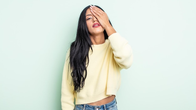 Pretty hispanic woman looking sleepy, bored and yawning, with a headache and one hand covering half the face