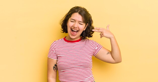 Pretty hispanic woman looking unhappy and stressed suicide gesture making gun sign with hand pointing to head