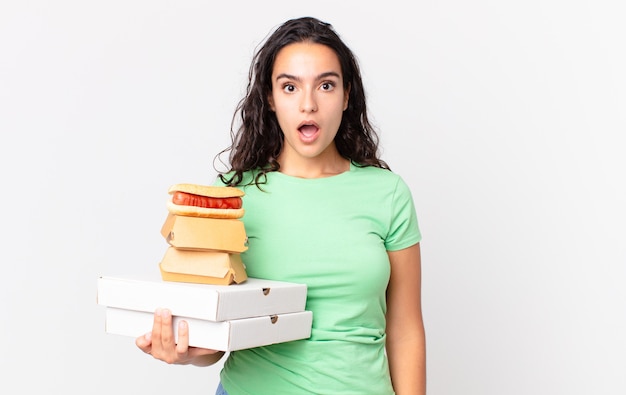 Pretty hispanic woman looking very shocked or surprised and holding take away fast food boxes