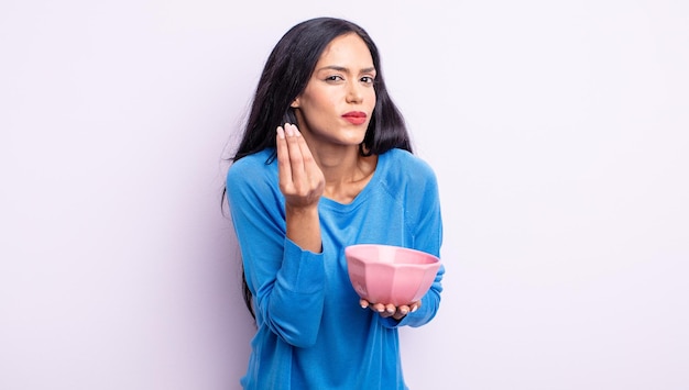 Pretty hispanic woman making capice or money gesture, telling you to pay. empty bowl concept