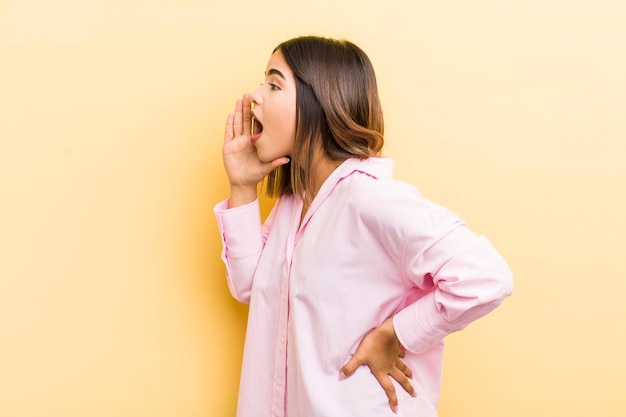 Pretty hispanic woman profile view looking happy and excited shouting and calling to copy space on the side