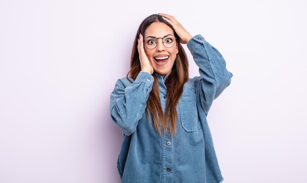 Pretty hispanic woman raising hands to head, open-mouthed, feeling extremely lucky, surprised, excited and happy