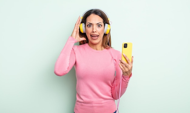 Pretty hispanic woman screaming with hands up in the air. smartphone and headphones concept