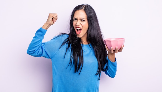 Pretty hispanic woman shouting aggressively with an angry expression. empty bowl concept