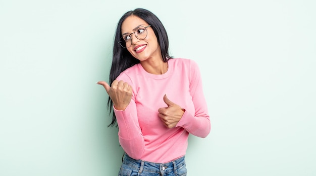 Pretty hispanic woman smiling cheerfully and casually pointing to copy space on the side, feeling happy and satisfied