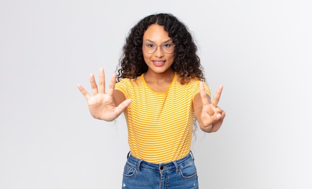 Pretty hispanic woman smiling and looking friendly, showing number seven or seventh with hand forward, counting down