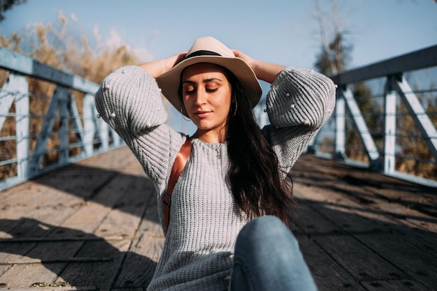 Pretty Hispanic woman wearing a hat relaxing outside in the sun with her arms up