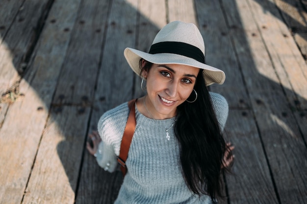 Pretty Hispanic woman wearing a hat sitting on a wooden floor and smiling at the camera