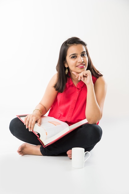 Pretty Indian Asian College Girl studying from book while sitting over white background