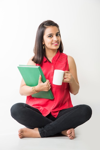 Pretty Indian Asian College Girl studying from book while sitting over white background