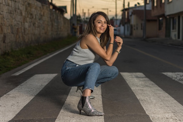 Pretty latin single woman portrait outdoors wearing jeans squatting over pedestrian crosswalk Selective focus